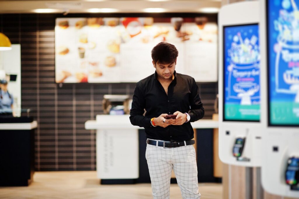Client at a fast food restaurant using floor-standing digital signage next to a digital menu board in Malaysia for a seamless purchasing experience